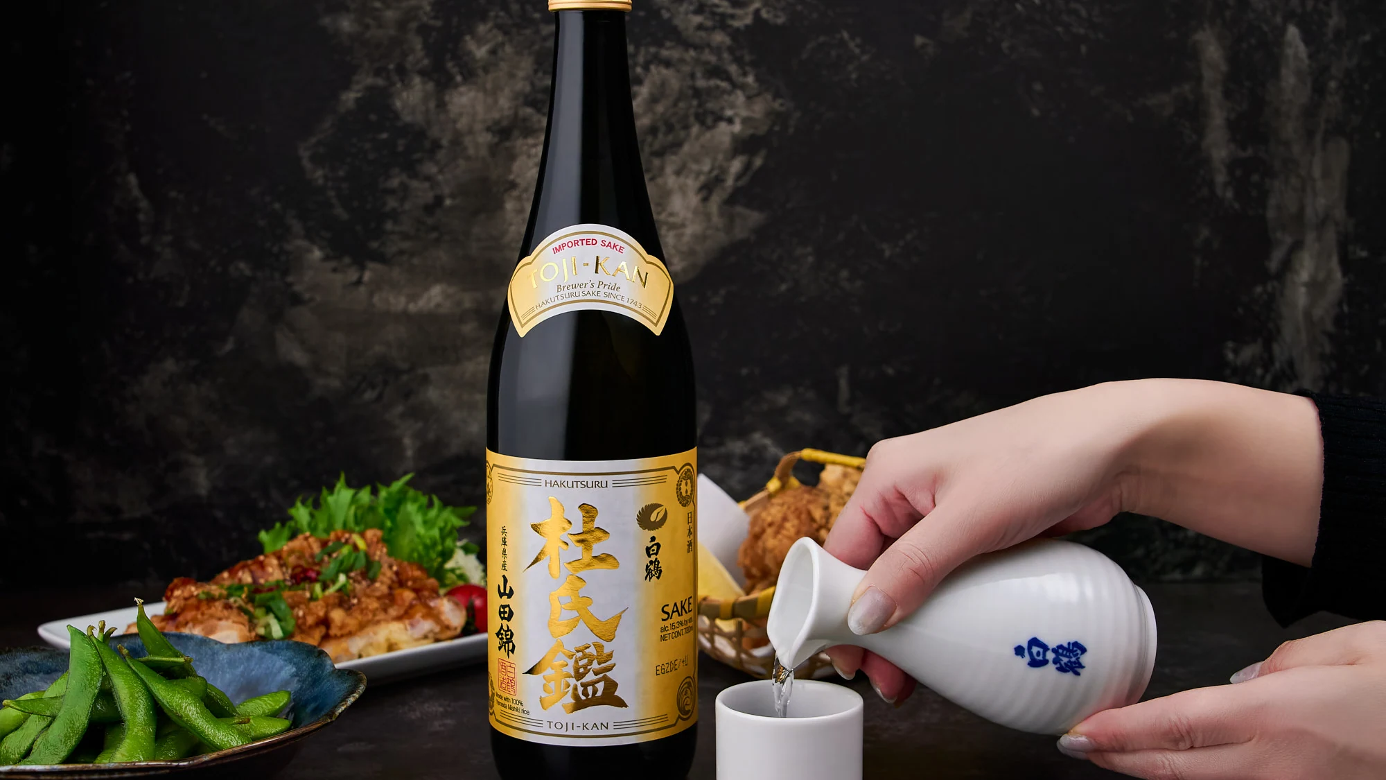 日本料理と酒瓶を囲み、徳利から酒を注ぐ様子