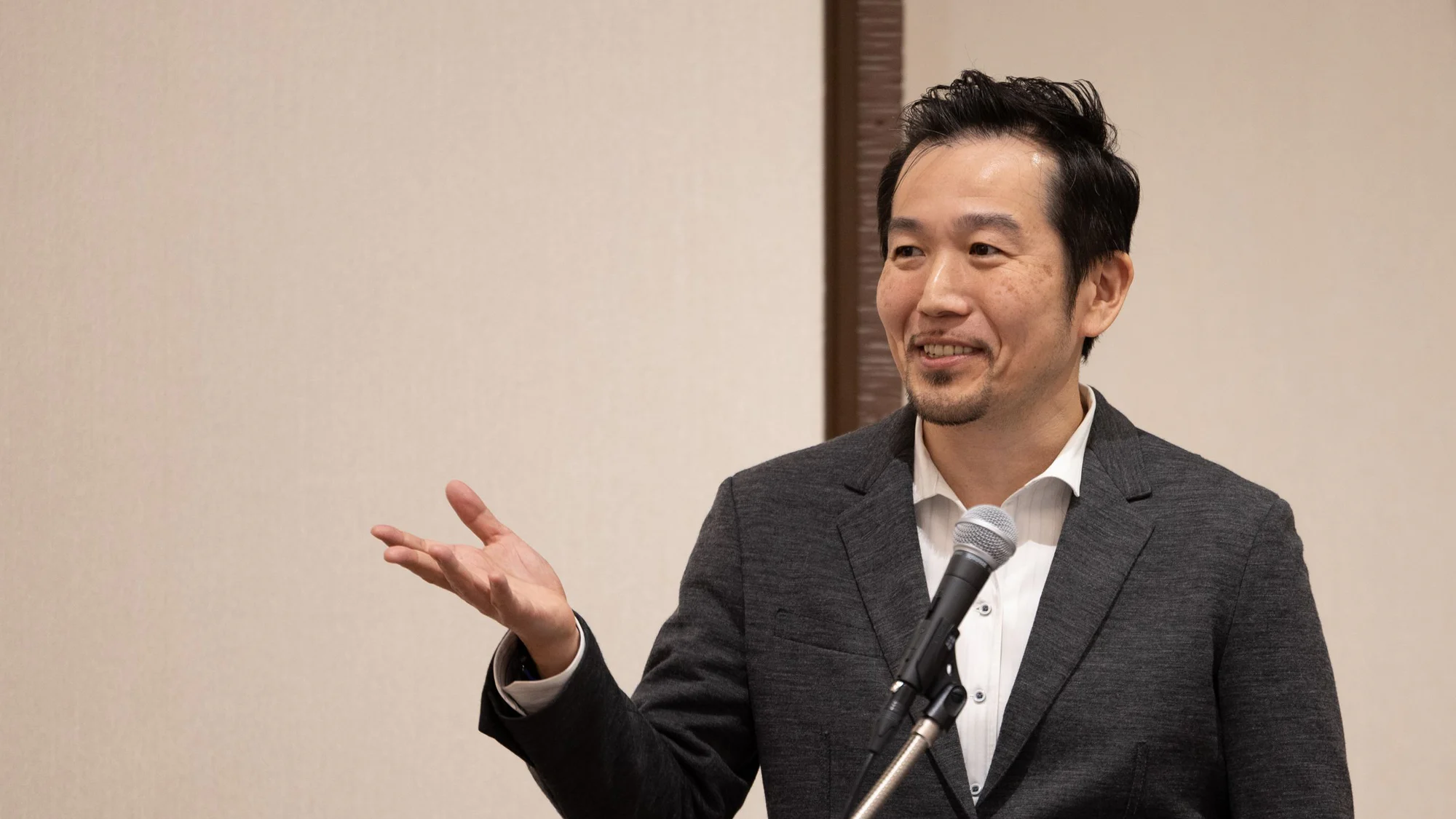 マイクを手に、身振りを交えながら聴衆に話すマーク・マツモト