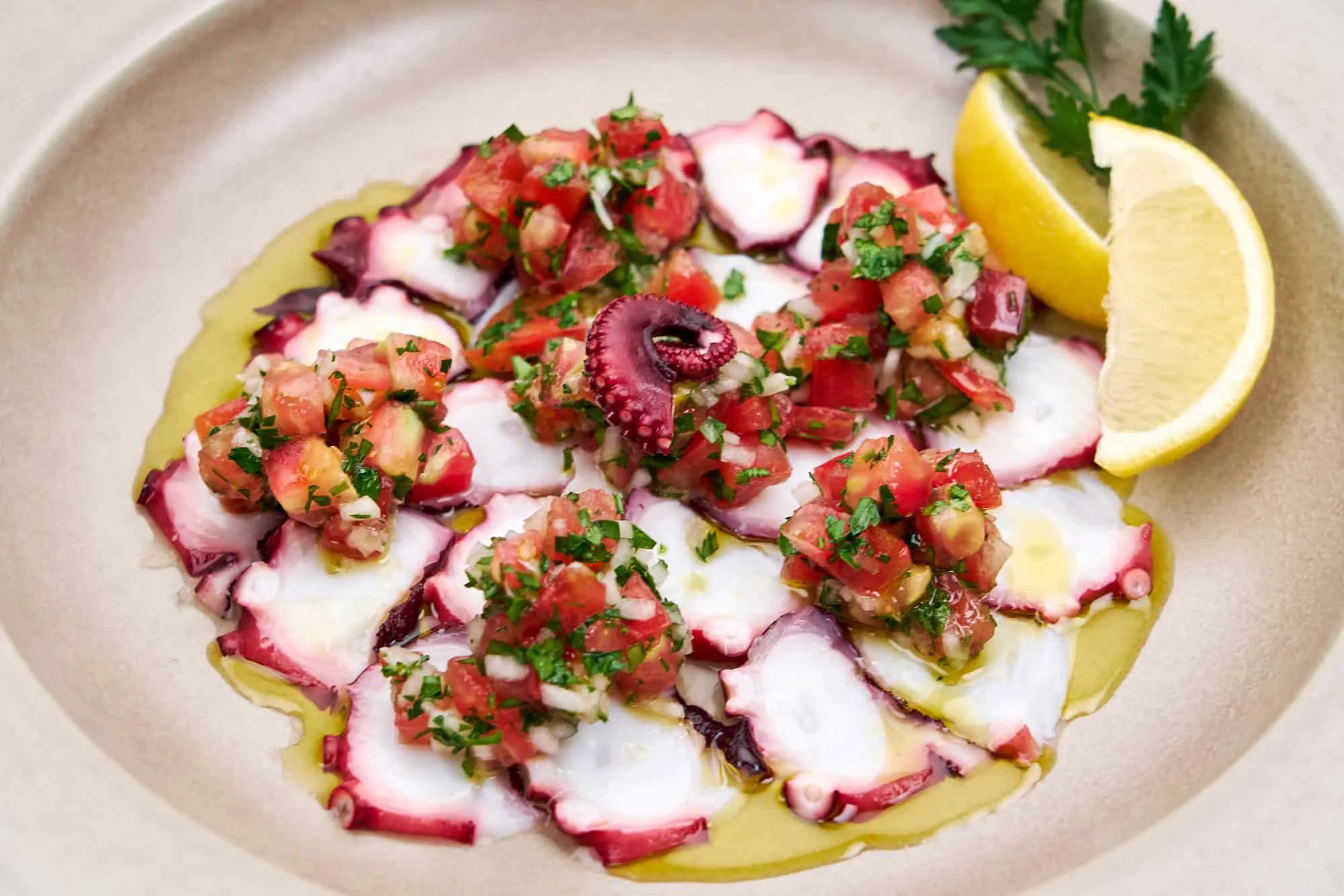Octopus carpaccio arranged with tomatoes, herbs, and citrus on a dark plate