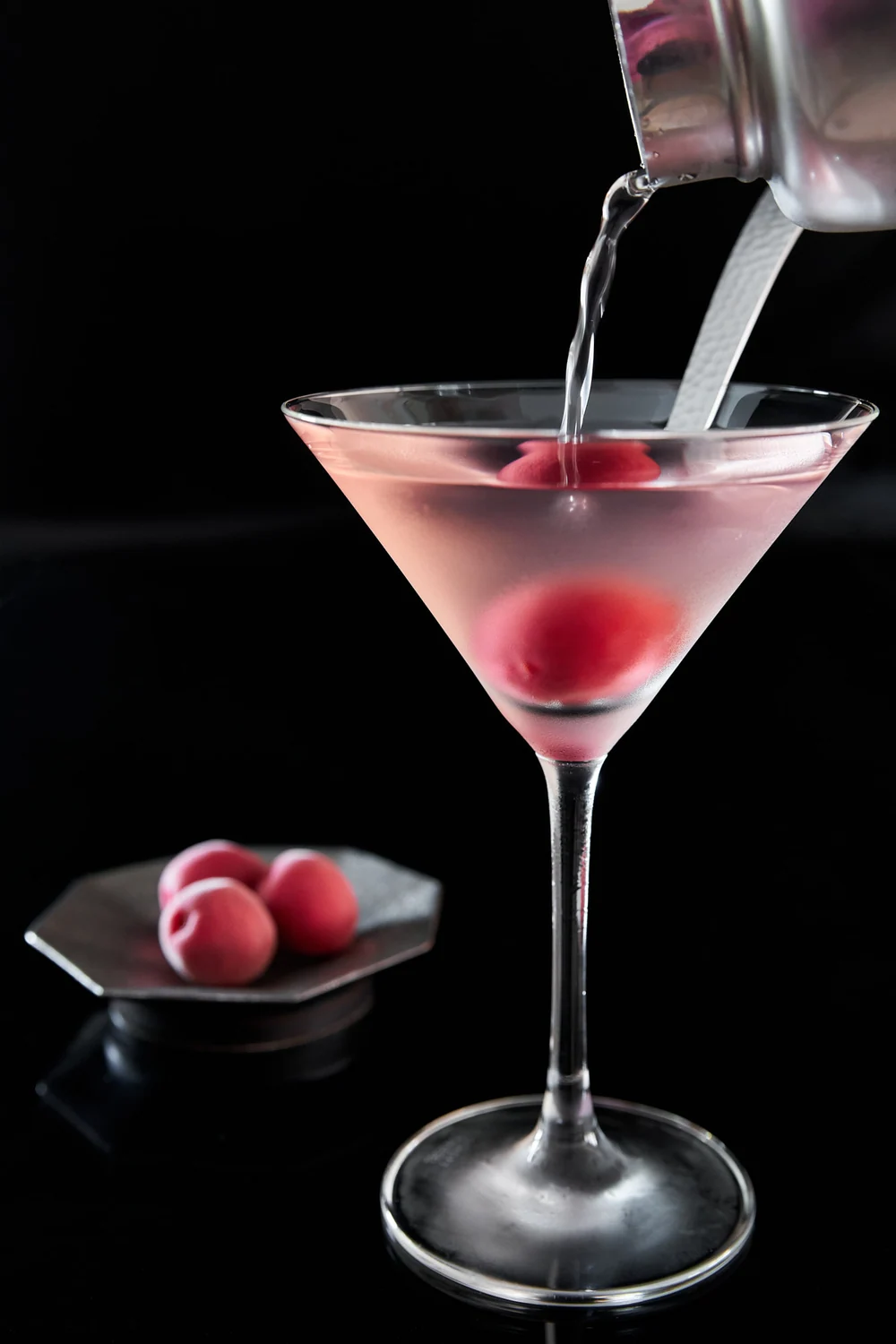 A pale pink ume martini being poured against a black background
