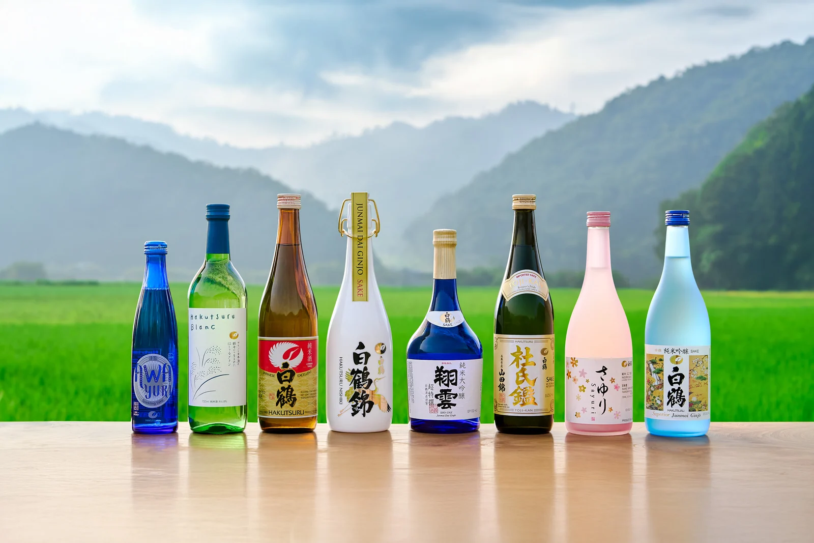 A range of Hakutsuru sake bottles arranged in front of rice fields